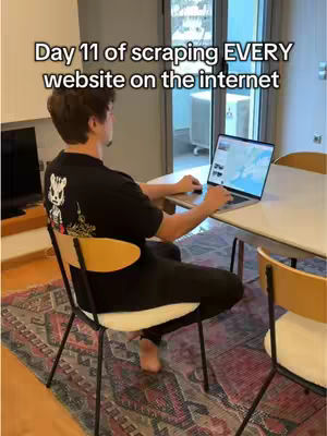 A man sits at a table facing a laptop with a map display. The scene is set in a well-lit room with a view of the outside through a glass door. Additional text is overlaid as a hook. The overall focus is on the creator multitasking.