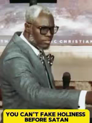 The image shows a man in a suit, wearing glasses, with grey and white hair. He has a serious expression. A yellow bar at the bottom says 'YOU CAN'T FAKE HOLINESS BEFORE SATAN'. Behind him is a light-colored background with text.