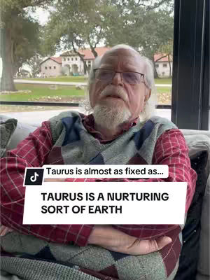 An older man with a white beard and glasses sits on a couch, looking at the camera. He is wearing a red and black patterned shirt with a dark blue vest. A white banner overlay reads, Taurus is a nurturing sort of earth.