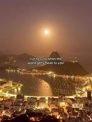 An aerial view of a city at dusk or dawn, with a body of water in the foreground and a large mountain in the background. The sky is filled with a soft, warm glow, and the city lights twinkle. Text overlayed reads, 'run to God when the world gets mean to you.'