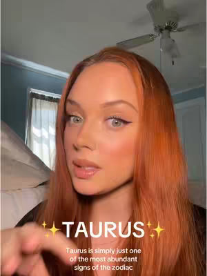 A young woman with long auburn hair and makeup is centered in the frame, with a soft-focus background suggesting a room, possibly a bedroom. The woman appears to be speaking, and overlaid on the image are the words 'TAURUS' in large, stylized text, along with descriptive text about the sign and gold stars. Her hand is extended towards the viewer.