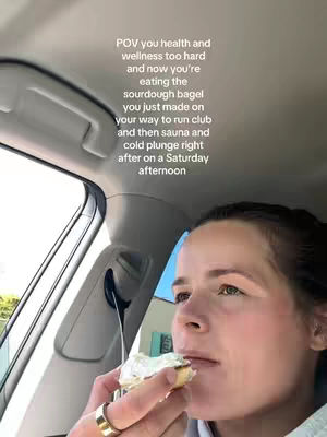 A woman inside a car is eating a bagel, shot from a low angle. Text overlay is on the top. The lighting is natural from the car.