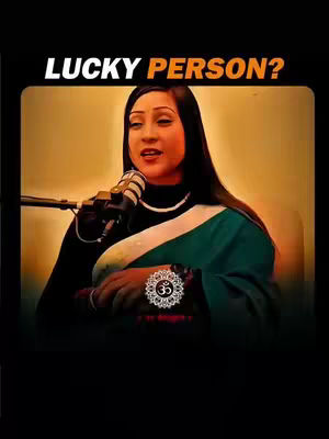 A woman with long dark hair wearing a black top and a teal and green patterned scarf is speaking into a microphone. The image has a dark border and the words 'LUCKY PERSON?' at the top.