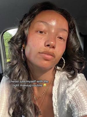 A selfie shows a young woman with dark hair, light skin, and hoop earrings. She's wearing a white, lacy top and a necklace with multiple strands. The background is somewhat out of focus, suggesting she might be in a car or near a window. A text overlay reads, 'never saw myself with the right makeup routine 🥺'.