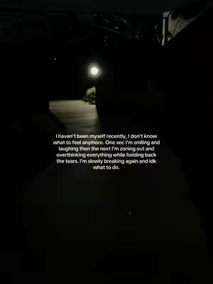 A dark, slightly blurry image of a nighttime outdoor scene, likely a road or driveway. A bright, distant light source, possibly a street lamp or an illuminated building, is visible, casting a soft glow that contrasts with the surrounding shadows. Text overlayed on the image displays a personal message in a white font.