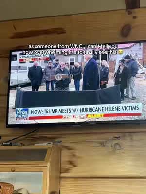 The image shows a television screen displaying news coverage of Donald Trump meeting with Hurricane Helene victims. A group of people, including Trump and various officials, are standing in front of what appears to be a podium. The text overlay states, 'as someone from WNC, I can't tell you how overwhelming it is to finally see this.' The foreground includes a wooden surface that presumably supports the television.
