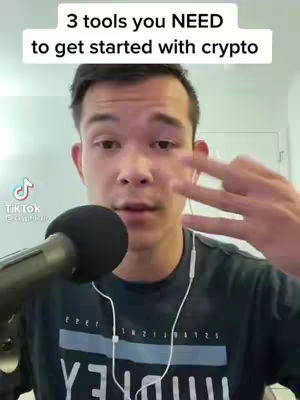 A man is centered in the frame, with a microphone prominently in front of him. He wears a dark t-shirt with white text. Above him is a white rectangular box with rounded edges with text over the image. He is gesturing with his fingers up.