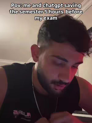 A selfie-style video with a young man looking down and to the left. He is wearing a dark, sleeveless shirt and a silver chain. The background is dimly lit, and text is overlaid at the top. The man has a beard and short, dark hair.