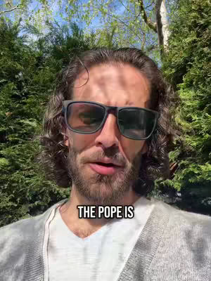 A man wearing sunglasses is centered, with his face filling the frame. Text overlay indicates, 'THE POPE IS' The background is a dense formation of green trees and foliage, and a bright sky is visible above the trees.