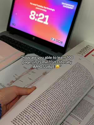 A person's hands are holding an open book with densely printed text in the foreground. Behind the book, a laptop displays the time 8:21 on its screen, reflecting an illuminated and colorful interface. The background includes a table, with a few more books titled Anatomy.