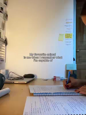 The image shows a desk with papers and a laptop, a woman's hand is writing in a notebook. Text overlayed reads: My favourite animal is me when I remember what I'm capable of