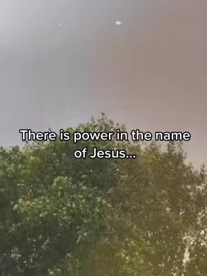 The image shows a view of a tree with vibrant green leaves. Above the tree, the sky is a gradient of gray. Text overlayed on the image reads, 'There is power in the name of Jesus...'