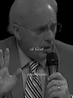 A grayscale image shows a man speaking, holding a microphone in front of a black background. The man is wearing glasses, a suit jacket, and a striped tie. Text overlays read 'of God' and the handle of the video creator.