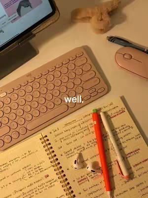 A top-down shot of a desk with study materials: a pink keyboard, notebook, pens, earphones, and a digital tablet.