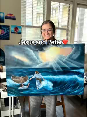 A woman with glasses holds a painting depicting Jesus walking on water with Peter, with an overall warm or inspirational color palette. The painting, held in front of her, is the primary focus, with a background showing an interior space with an open window. The woman is smiling, facing forward, and the scene is well-lit.