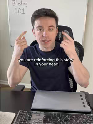 A man in a navy blue t-shirt gestures with his index fingers towards his temples. Text overlays on the image, and a keyboard, laptop, and part of a whiteboard are visible.