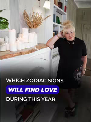 The cover image shows an older woman with blonde hair standing in an interior setting. She is wearing a black dress and leaning against a white surface, possibly a fireplace mantel. In the background, there is a white shelf with books and decorative candles. The text overlay includes the title "WHICH ZODIAC SIGNS WILL FIND LOVE DURING THIS YEAR".