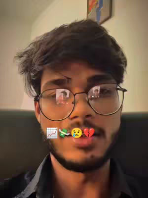 A selfie-style image of a young man wearing glasses. He has dark hair and a beard. Text and emojis are placed over his mouth. The background seems to be an indoor setting, lightly lit.