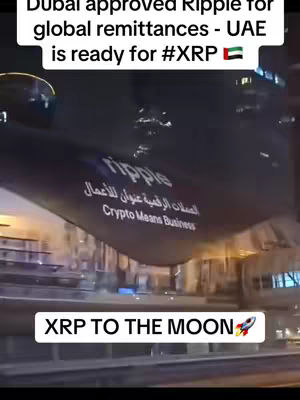 A night-time city scene with a dark banner reading "Ripple" and "Crypto Means Business" in both English and Arabic. Below, a text overlay reads "XRP TO THE MOON" with a rocket emoji.