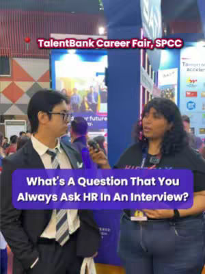 A video cover featuring two people at a career fair. A man in a suit and a woman in a black t-shirt are shown. The woman is holding a microphone and the man is looking at her. A purple bar at the bottom of the image reads: "What's A Question That You Always Ask HR In An Interview?"