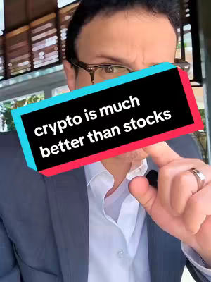 A man with glasses holds a sign that says "crypto is much better than stocks". He is wearing a white shirt and a dark gray blazer. The background is out of focus.