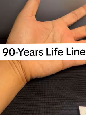 The image shows a close-up of a person's open hand, palm facing upwards. The skin tone appears to be light to medium. The background is a dark, textured fabric. A white rectangular bar with black text, "90-Years Life Line", is overlaid near the middle of the image, positioned just below the hand.