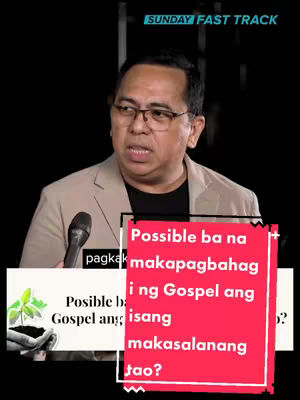 A man in a light-colored suit jacket and glasses is speaking into a microphone. Behind him is a black background. Overlayed on the image are text boxes, with a white and red color scheme.
