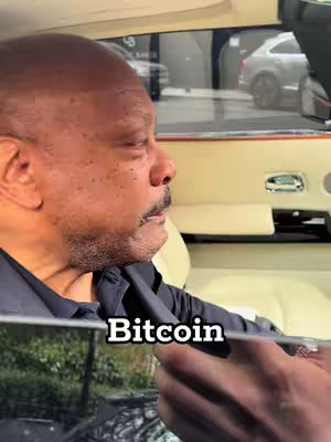 A man is inside of a car, with the main focus on his face. There is a black text overlay that partially blocks the vision of the environment outside as the text covers the person's face.