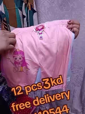 A person is holding up a pair of light pink shorts with a cartoon graphic of a girl playing a guitar on one side. The shorts are in front of a patterned background and the person's hands and arms are visible holding them out. Text in orange is overlaid on the image, advertising the shorts alongside their price and providing a way to contact the seller.
