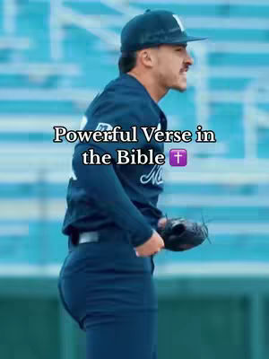 A man in a baseball uniform is showcased on a baseball field in sunlight. The man is wearing a baseball cap, a dark-colored baseball jersey with white lettering, and dark-colored pants. He is wearing a black glove and is looking to the right with a slight smile. Text overlayed on the image says "Powerful Verse in the Bible" in a stylized font.