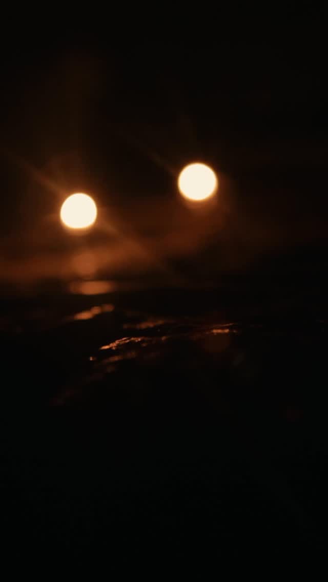 A dark image featuring two glowing, blurred orbs against a shadowy background. There's a suggestion of a landscape or water in the lower portion, also obscured by shadows.