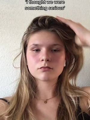 A young woman with light skin and long blonde hair looks directly at the camera with a slightly pained expression. She has red cheeks and a small gold pendant. Her hand is raised to her head touching her hair, with text overlaid at the top.