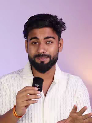 A man with dark hair and a beard is the central figure, holding a small black microphone close to his chin. He is wearing a white textured shirt. The background a gradient of colors.