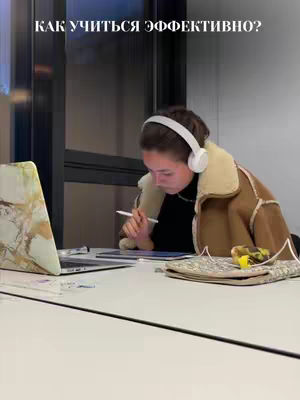 A woman wearing headphones and a coat is seated at a desk, leaning over a tablet and laptop. The desk surface is white. Text in white appears at the top of the background