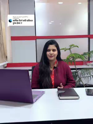 A woman sits at a desk in a modern office setting, with a laptop, notebook, and phone in front of her. She is wearing a maroon long-sleeved shirt, a red lanyard, and looking directly at the camera. A speech bubble is visible in the upper left corner.