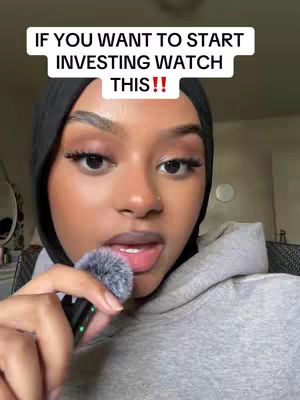 A woman with dark hair and a hijab is holding a microphone close to her mouth in a close-up shot. She appears to be speaking directly to the camera. The background is slightly blurred, suggesting an indoor setting. Text overlay is positioned above her head.