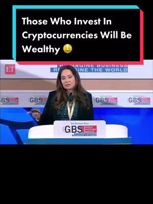 A woman in a black blazer stands at a lectern on a stage. The background includes a screen advertising 'Imagine Business Reimagine the World.' The text overlay, in a black rectangle with red and blue borders, reads: 'Those Who Invest In Cryptocurrencies Will Be Wealthy.' The image has a professional, informational feel.
