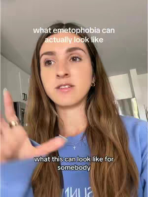 A woman with long brown hair is in a well-lit room. Her eyes are gazing slightly upward, and her hand is raised with fingers extended, appearing to point. Text overlays are present, and she's wearing a blue sweatshirt. The background suggests a home interior.