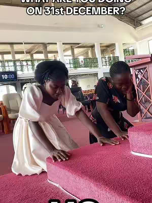 Two women are kneeling on a pink carpeted surface. One is wearing a cream-colored dress, and the other is in a black floral patterned top. Text overlayed states 'WHAT ARE YOU DOING ON 31st DECEMBER?'