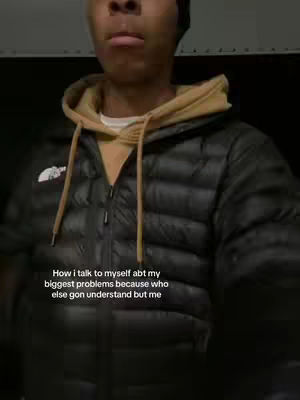 A medium shot of a young man from the chest up, facing the camera with a slightly somber expression. He wears a black beanie, a light tan hoodie beneath a black puffer jacket. The background is a dark, blurred space, and text overlay lies below the neck.