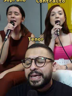 The cover image is a selfie style shot featuring three people singing into microphones. The main subject is a man with glasses in the foreground, with two women behind him to each side. The women are singing into microphones and the man is singing as well, they all are looking towards different directions. The text overlay indicates what vocal part each of them are singing: Soprano, Contralto, and Tenor.