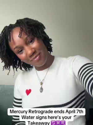 A woman with dark, textured hair and a warm expression looks towards the camera. She wears a white sweater with black stripes along the sleeves and a red heart on the chest. Below her is a graphic with text in white overlay.