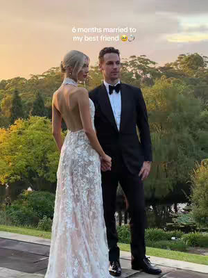 The cover image features a couple in wedding attire. The bride is wearing a white, backless, lace wedding dress, and the groom is in a black tuxedo with a bow tie. They are holding hands, with a blurred green background of trees and a sunset.