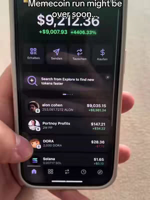 A person's hand holding a smartphone, displaying a cryptocurrency app interface. The screen shows financial data related to several cryptocurrencies including 'alon cohen', 'Portnoy Profits', 'DORA', and 'Solana'. The phone's interface includes purple and dark gray color scheme, indicating the portfolio value with a large green increase. The background appears to be a carpeted surface.