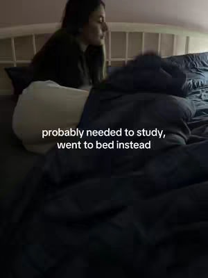 A young woman is lying in bed, partially covered by a blue blanket. The image is composed with a soft focus, suggesting a cozy or relatable scene. Text overlay emphasizes a common student experience of choosing bed over studying.