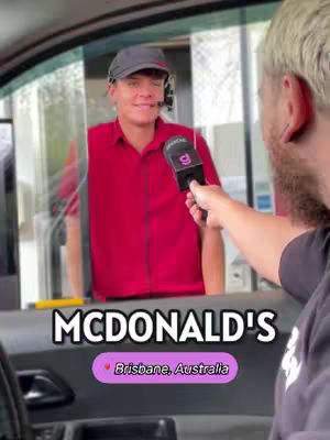 A person wearing a black cap and red shirt is being interviewed through the window of a McDonald's drive-through. The interviewer is holding a microphone. The McDonald's logo and location are featured in the lower portion of the image.