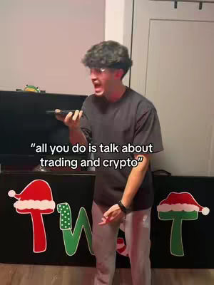 A man with curly hair and glasses is on a phone call. Text overlayed on the image reads, "all you do is talk about trading and crypto." The background is a room with black furniture and Christmas decorations.