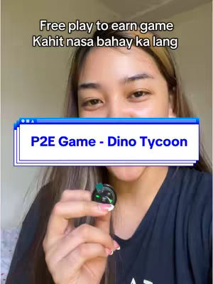 A woman is centered in the frame, holding a small black device, likely a game component. Above her, text overlays read, encouraging viewers to play a free, play-to-earn game. A blue and white text banner highlights the game's name: 'P2E Game - Dino Tycoon'. The background is a blurred interior, suggesting casual, at-home content creation.