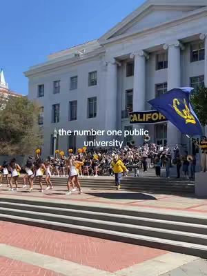 A daytime shot of a university campus with a large classical-style building in the background. In front, there are steps leading up to the building with students and a marching band. Cheerleaders are visible to the left, and a flag with a design is waving on the right. Text overlay says 'the number one public university'. The overall scene is bright and collegiate.