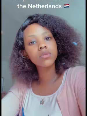 An image of a young woman looking up with a slightly melancholic expression. She has a dark complexion and curly dark hair. She is wearing a white top and a pink sweater or cardigan. The background is blurry, with the focus on the woman.